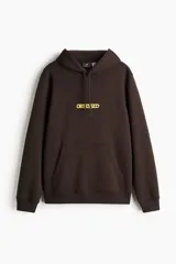 Canguro marrón de peso medio, con capucha de doble capa con cordón de ajuste, bolsillo canguro frontal y estampa con la palabra "OBSESSED" en amarillo en el pecho. Presenta puños y bajo acanalados.