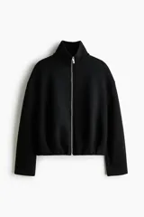 Campera negra de efecto neopreno, con cuello chimenea, cierre frontal completo y hombros caídos. Presenta un diseño holgado con pliegues en el bajo y mangas largas.