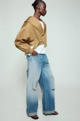 Chaqueta corta de Zara confeccionada en mezcla de algodón, con cuello solapa, manga larga con hombro caído y puños elásticos. Presenta un diseño cruzado con cierre de hebilla metálica lateral y forro interior a tono.