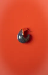 Aros tipo argolla pequeña con diseño semicircular, combinando una pieza de resina jaspeada en tonos azul oscuro con un detalle metálico dorado brillante.