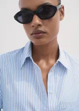 Camisa de corte crop y diseño recto, con estampado de rayas verticales en azul y blanco. Presenta cuello camisero, bolsillo en el pecho, cierre frontal con botones y mangas tres cuartos.