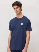 Camiseta de corte regular fit color azul marino, de manga corta y cuello redondo, confeccionada en 100% algodón orgánico, con un pequeño estampado de una cruz blanca en el pecho.
