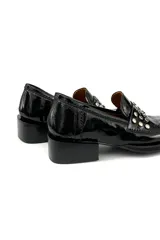 Mocasín de cuero charol negro con detalle de apliques metálicos plateados en la parte delantera y taco bajo cuadrado.