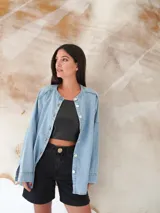 Camisa de denim liviano con lavado azul, cuello mao, manga larga y cierre frontal con botones de nácar. Presenta un corte holgado y oversize con ruedo redondeado.