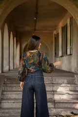 Blusa de lino con estampado artístico en tonos tierra, verdes y azules. Presenta un corte holgado con mangas abullonadas, puños elásticos y un cordón ajustable en el ruedo frontal para entallar la cintura.