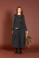 Chaleco gris oscuro con diseño a cuadros sutil, corte recto, cierre frontal con botones y bolsillos con tapa solapa. Presenta un detalle de volado asimétrico en el bajo.