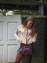 Campera color crema de tejido de punto, con cuello tortuga, mangas largas y cierre frontal con cremallera color borgoña. Presenta bolsillos ojal con pespunte en la parte delantera.