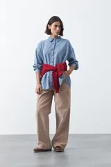 Camisa de jean en tencel con silueta amplia, hombros caídos, cuello clásico y cierre frontal con botones. Presenta ruedo curvo con tajos laterales y pliegue en la espalda.