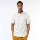 Camisa de manga corta color blanco con diseño estampado de pequeñas palmeras negras, cuello camisero y cierre frontal de botones.