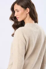 Buzo tejido de punto en color beige, con cuello redondo, mangas largas y puños acanalados. Presenta un delicado diseño bordado con motivos florales dispersos en el frente y una etiqueta de cuero sintético en el ruedo.