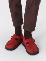 Slipper tipo guillermina confeccionada en gamuza roja, con plataforma de goma negra y doble hebilla ajustable. Presenta un pespunte decorativo en contraste en el borde inferior y cuenta con interior recubierto en cuero.