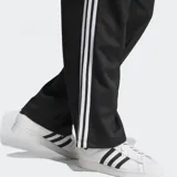 Pantalón de jogging negro Adidas Adicolor Firebird de corte holgado, con tres tiras blancas verticales a lo largo de cada pierna.