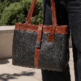 Bolso tipo tote de cuero color marrón con detalles en negro. Tiene doble asa de hombro y correa extraíble regulable. Incluye cierre principal y bolsillo interior.