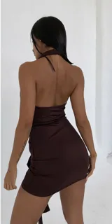 Vestido corto color marrón, con cuello halter, ajuste al cuerpo y detalle de nudo lateral en la falda con caída asimétrica.