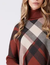 Polera estilo poncho de corte oversize, con cuello alto tejido y mangas largas con puños elásticos. Presenta un diseño de estampado a cuadros en tonos bordó, beige y negro.