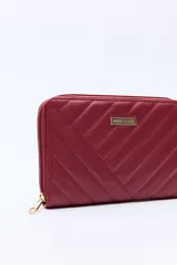 Billetera capitoneada en símil cuero color negro, con pespuntes en diagonal y cierre perimetral. Cuenta con un logo metálico dorado en el frente.