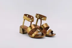 Sandalias negras de cuero con dos tiras horizontales sobre el pie y pulsera al tobillo con ojalillos y tachas. Taco cuadrado de 5 cm.