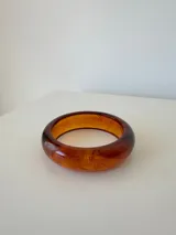 Pulsera rígida tipo brazalete de acrílico en tono ámbar con efecto marmolado.