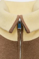 Chaqueta de punto con cierre frontal de cremallera, cuello alto, manga larga y bolsillos delanteros de plastrón. Presenta un diseño bicolor en tonos marrón y amarillo claro en cuello, puños y ruedo.