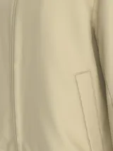 Campera de nailon estructurado color beige, con corte regular y cuello alto de canalé. Presenta cierre frontal de cremallera, bolsillos laterales, puños y bajo elásticos, y forro ligeramente acolchado. Incluye el logo de Calvin Klein bordado en el pecho.