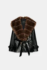 Trench corto Zara de efecto piel color negro, con cuello de solapa y aplicación de pelo sintético a contraste en color marrón. Cuenta con manga larga con trabillas en los puños, bolsillos delanteros y cinturón ajustable del mismo tejido.