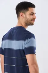 Remera de algodón con diseño de rayas horizontales en tonos azul marino, celeste y líneas finas en verde claro y amarillo pálido. Cuenta con cuello redondo y mangas cortas, con un pequeño bordado en el pecho.