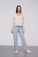 Chaqueta de algodón color beige, con diseño holgado, cuello tipo camisa, cierre frontal con botones metálicos y bolsillos frontales con solapa.