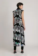 Chaleco largo de terciopelo negro con lentejuelas florales plateadas, sin mangas, con cuello tipo esmoquin, bolsillos delanteros y cinturón desmontable.