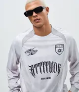 Remera de manga larga estilo deportivo con corte boxy, confeccionada en poliéster. Presenta cuello redondo, paneles laterales en tejido texturizado y estampados gráficos estilo tribal y lettering gótico en el frente.