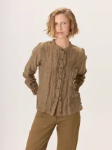Camisa de algodón color marrón oscuro, con cuello mao, cierre frontal con botones y detalle de volados en la tapeta. Presenta mangas largas con puños elásticos y diseño fluido.