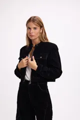 Chaqueta corta de terciopelo negro con efecto desgastado en tono azulado, cuello mao, cierre frontal metálico y bolsillos frontales con tapa y botón.