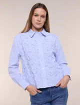 Camisa de algodón celeste con patrón de milrayas finas y aplicaciones florales en relieve deshilachado en el frente. Cuenta con cuello camisero tradicional, cierre frontal con botones, mangas largas con puños abotonados y corte semi holgado.