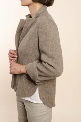 Chaqueta marrón de lana con cuello, solapa y bolsillos ojal. Forro solo en las mangas y terminaciones envivadas. Esquinas redondeadas y mangas con corte en puño que permiten transformarla en manga 3/4. Más larga en la espalda que en la delantera. Abrochadura con dos botones.