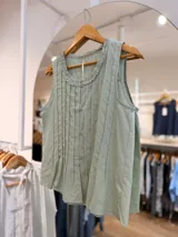 Blusa sin mangas color verde menta, con diseño de tablitas verticales en el frente, cierre frontal con botones al tono y cuello redondo decorado con un delicado volado fruncido.