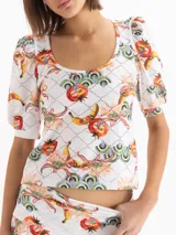 Remera blanca de punto con estampado full print colorido y textura suave, escote redondo profundo, mangas cortas con frunces y hombreras en la copa con puños ajustados, y corte al cuerpo.