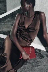 Bolso de hombro de formato rígido en piel color borgoña, con detalle de pespuntes que crean un patrón de cuadrícula. Posee triple compartimento y doble asa de hombro en cadena metálica dorada.