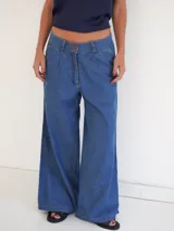 Pantalón palazzo de denim azul claro con pinzas en la cintura, bolsillos laterales y cierre frontal con botón.