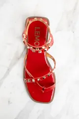 Sandalias rojas de charol con tiras finas, puntera cuadrada y cierre con hebilla al tobillo. Decoradas con tachas piramidales doradas.