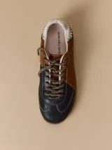 Championes de cuero con diseño tricolor en tonos negro, marrón y crema. Presentan cordones trenzados, costuras a la vista y detalle de pespuntes en el talón.