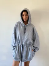 Vestido tipo hoodie oversize de color gris melange, con capucha, cordones ajustables en el cuello y en la cintura, y bolsillos laterales.