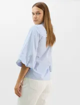 Camisa de algodón con patrón de rayas verticales, cuello camisero clásico y cierre frontal con botones. Presenta detalles metálicos aplicados en el frente y mangas, con mangas 3/4 abullonadas y ruedo recto.