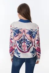 Camisa de lino de manga larga, con cuello y botones frontales. Presenta un estampado artístico y colorido en tonos rosados, azules y blancos, con motivos que recuerdan a escudos o medallones.