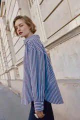 Camisa de corte clásico con cuello solapa y manga larga, confeccionada en tejido oxford con diseño de rayas verticales en azul y bordó. Presenta cierre frontal con botones y bajo con aberturas laterales.