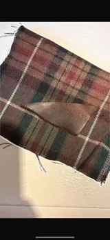 Cartera de mano con diseño clásico, confeccionada en tela escocesa de tonos tierra con detalles en cuero marrón.