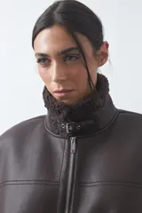 Chaleco de cuero sintético negro con interior y detalles de corderito en cuello, sisas y ruedo. Presenta cierre frontal completo y diseño holgado.
