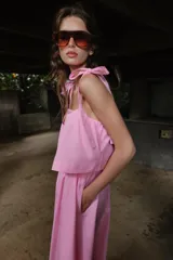 Vestido midi de color rosado con escote recto elástico y tirantes anchos con lazos ajustables. Presenta cintura elástica y bolsillos laterales ocultos en la costura.