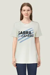 Remera blanca de manga corta y cuello redondo, de corte holgado. Presenta un estampado frontal con la frase "GARRA CHARRÚA" en color negro sobre líneas diagonales azules.