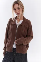 Cardigan de tejido de punto color marrón, con cuello solapa, cierre frontal de cremallera y diseño de trenzas. Cuenta con puños y dobladillo en rib elástico y un pequeño bordado en el pecho.