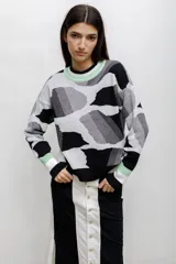 Buzo tejido en técnica jacquard con diseño geométrico abstracto en blanco, negro y gris. Presenta cuello redondo, puños y ruedo acanalados con detalles en color verde menta.