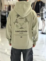 Canguro oversize verde claro con capucha y bolsillo tipo canguro. Presenta un gran estampado en la espalda de una pelota de fútbol con la inscripción "Azteca" y texto "Last-minute" junto con tres estrellas.